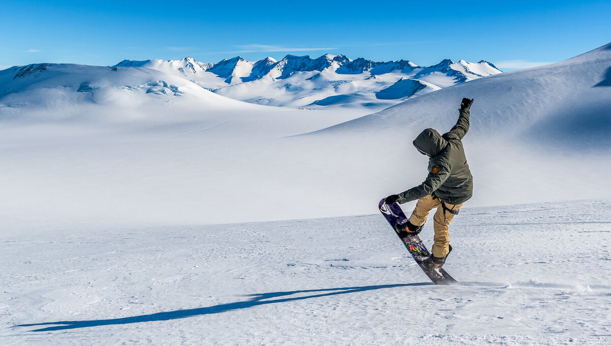 A snowboarder pops a wheelie against a pristine landscape